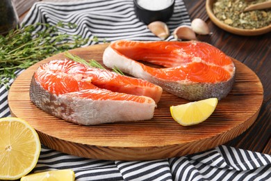 Photo of Board with fresh salmon steaks and lemon on wooden table, closeup