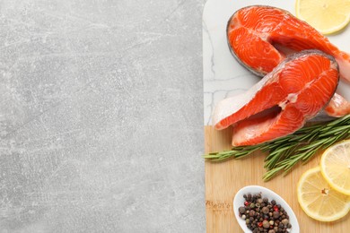 Photo of Board with fresh salmon steaks, peppercorns, rosemary and lemon on grey textured table, top view. Space for text