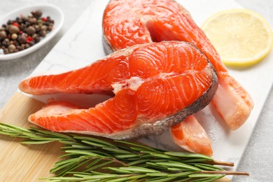 Photo of Board with fresh salmon steaks, peppercorns, rosemary and lemon on grey table, closeup