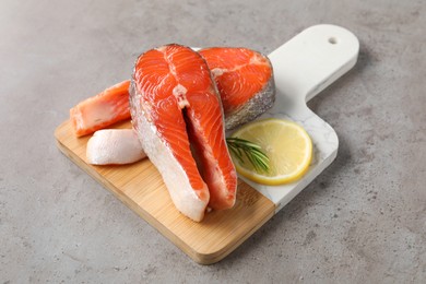 Photo of Board with fresh salmon steaks, rosemary and lemon on grey textured table, closeup