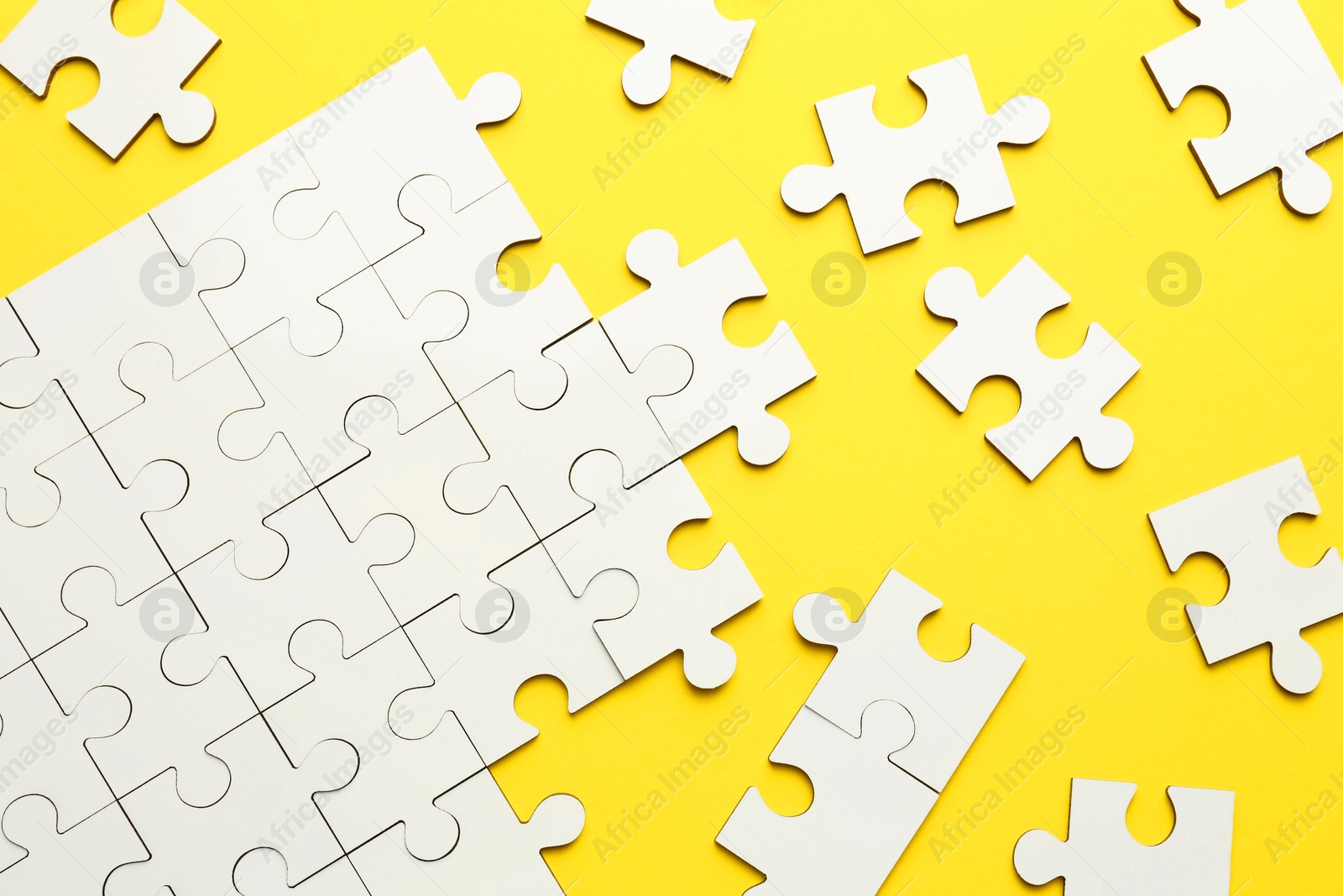 Photo of White puzzle pieces on yellow background, top view