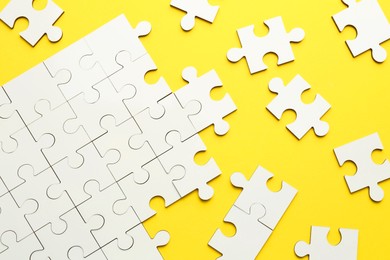 Photo of White puzzle pieces on yellow background, top view