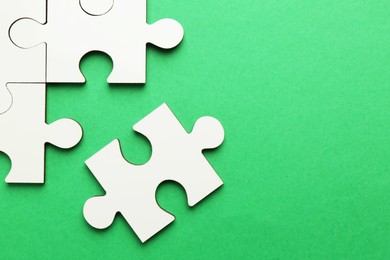 Photo of White puzzle pieces on green background, top view. Space for text