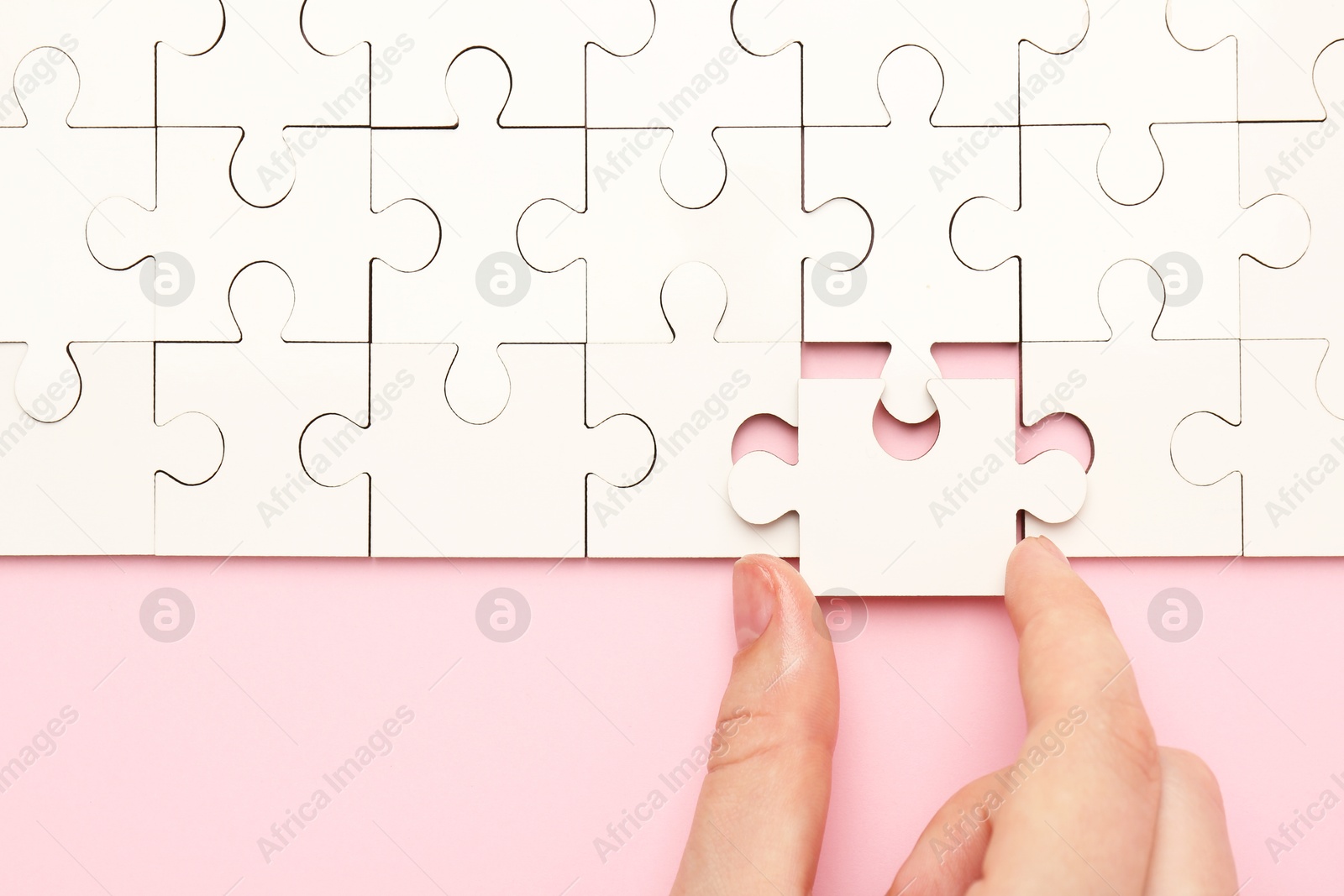 Photo of Woman solving white puzzle on pink background, closeup