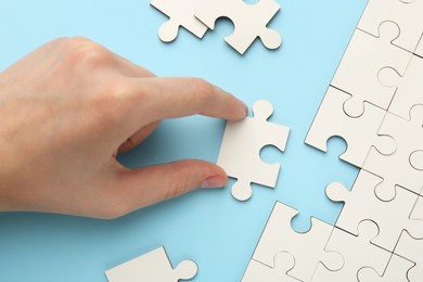 Woman solving white puzzle on light blue background, closeup