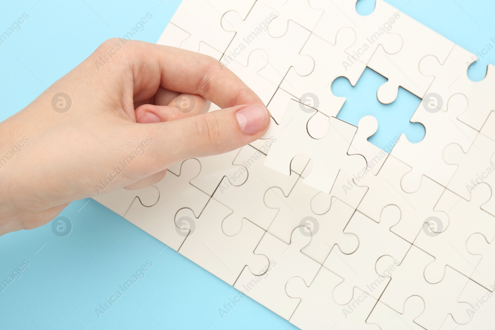 Photo of Woman solving white puzzle on light blue background, closeup