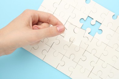 Photo of Woman solving white puzzle on light blue background, closeup