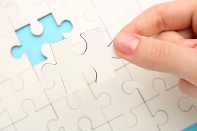 Photo of Woman solving white puzzle on light blue background, closeup