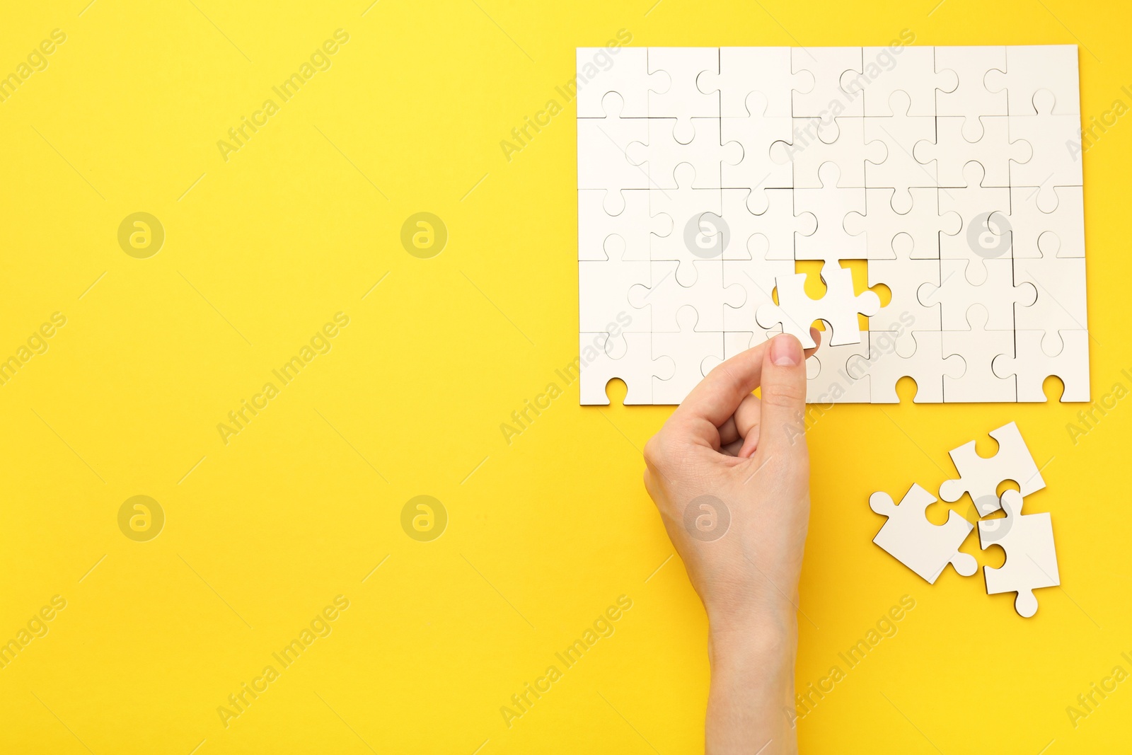 Photo of Woman solving white puzzle on yellow background, closeup