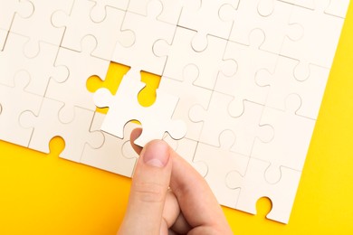 Woman solving white puzzle on yellow background, closeup