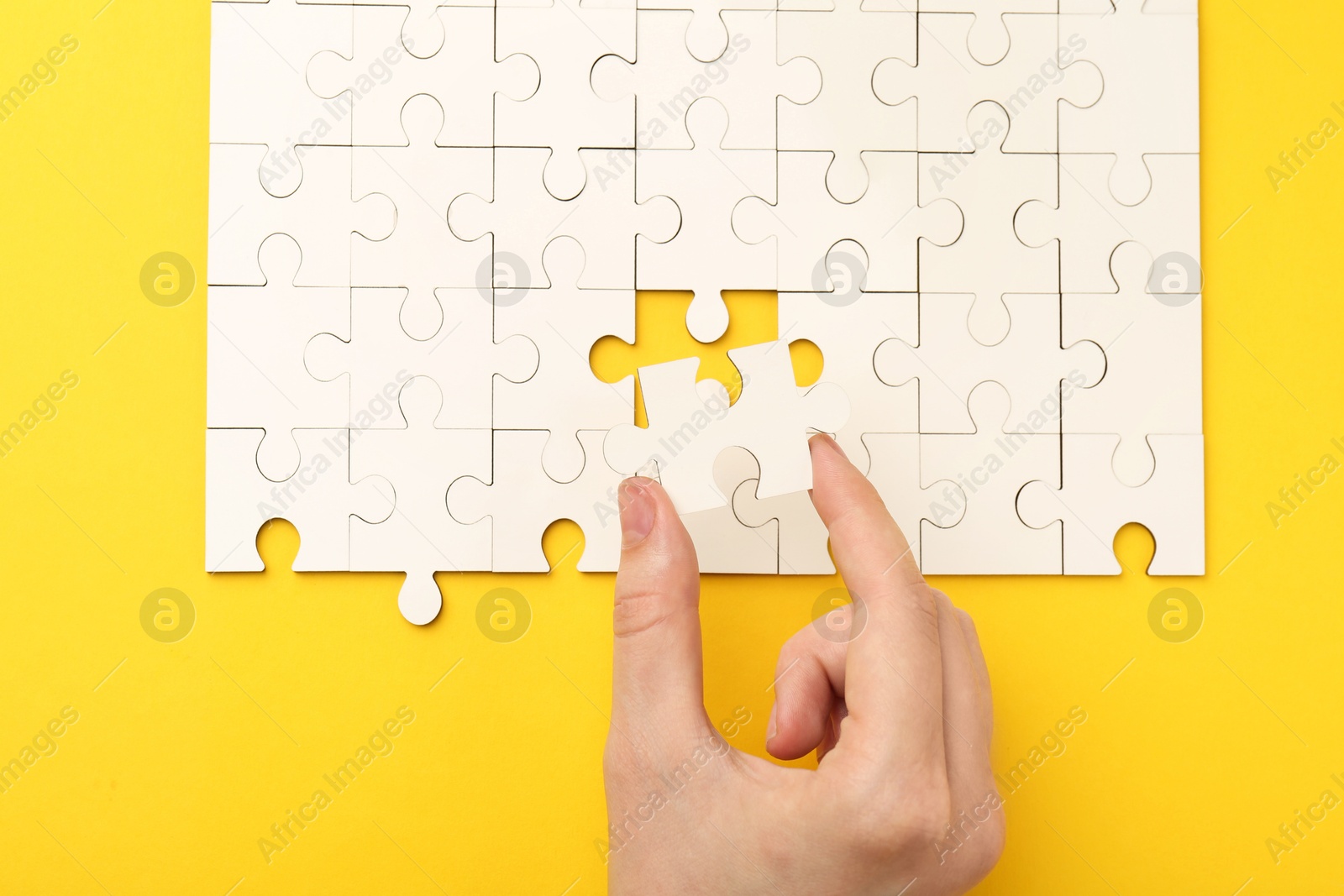 Photo of Woman solving white puzzle on yellow background, closeup