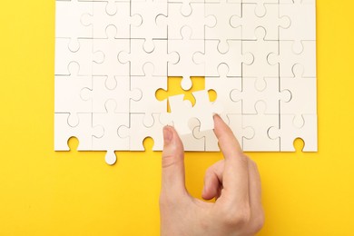 Photo of Woman solving white puzzle on yellow background, closeup