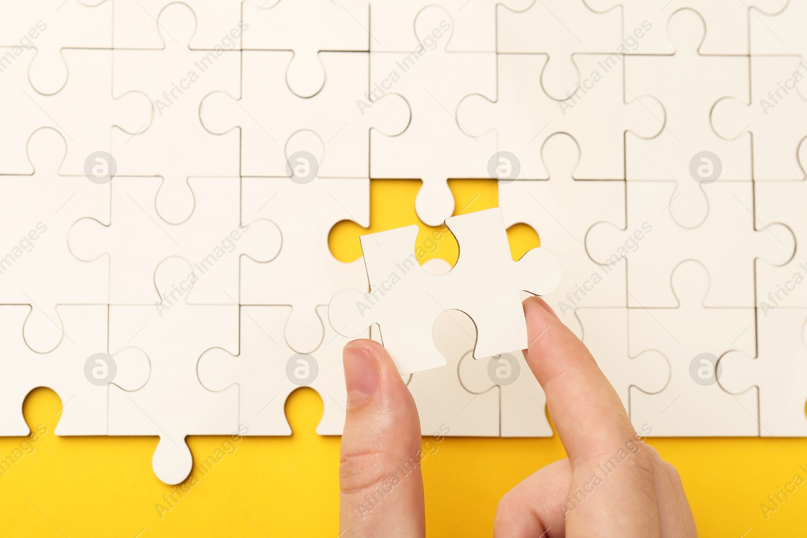 Photo of Woman solving white puzzle on yellow background, closeup