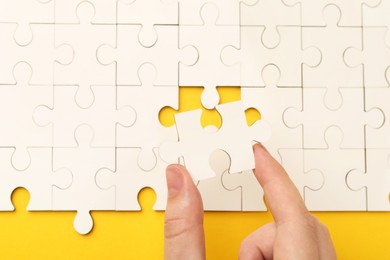 Woman solving white puzzle on yellow background, closeup