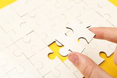 Woman solving white puzzle on yellow background, closeup