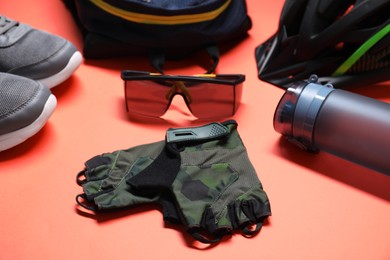 Bicycle helmet, backpack, sneakers, fingerless gloves, thermo bottle and goggles on coral background, closeup