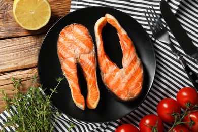 Photo of Tasty grilled salmon steaks, tomatoes, lemon, thyme and cutlery on wooden table, flat lay