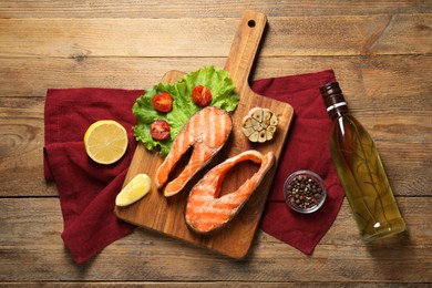 Tasty grilled salmon steaks, vegetables, spices, oil and lemon on wooden table, flat lay