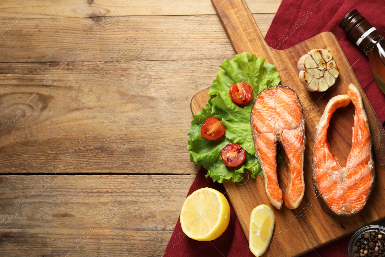 Photo of Tasty grilled salmon steaks, vegetables, spices, oil and lemon on wooden table, flat lay. Space for text