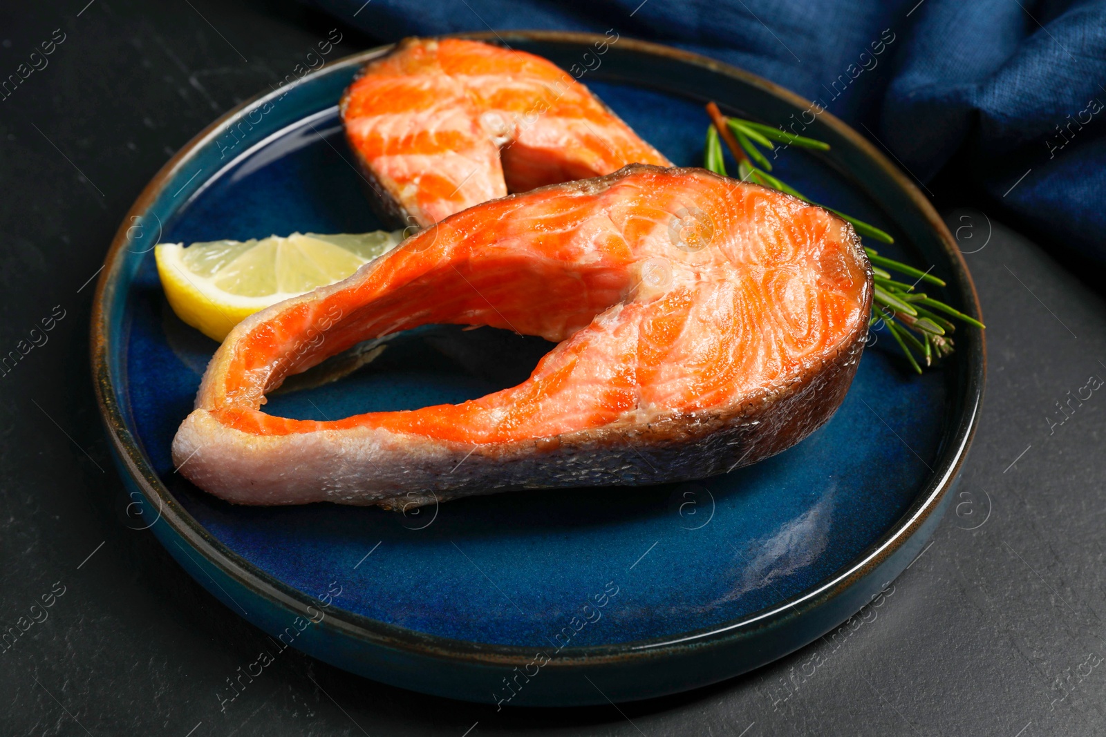 Photo of Tasty grilled salmon steaks, lemon and rosemary on black table, closeup