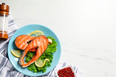 Photo of Tasty grilled salmon steaks, lettuce, lemon and spices on white marble table, flat lay. Space for text