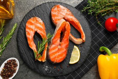 Photo of Tasty grilled salmon steaks, vegetables, oil and spices on gray textured table, flat lay