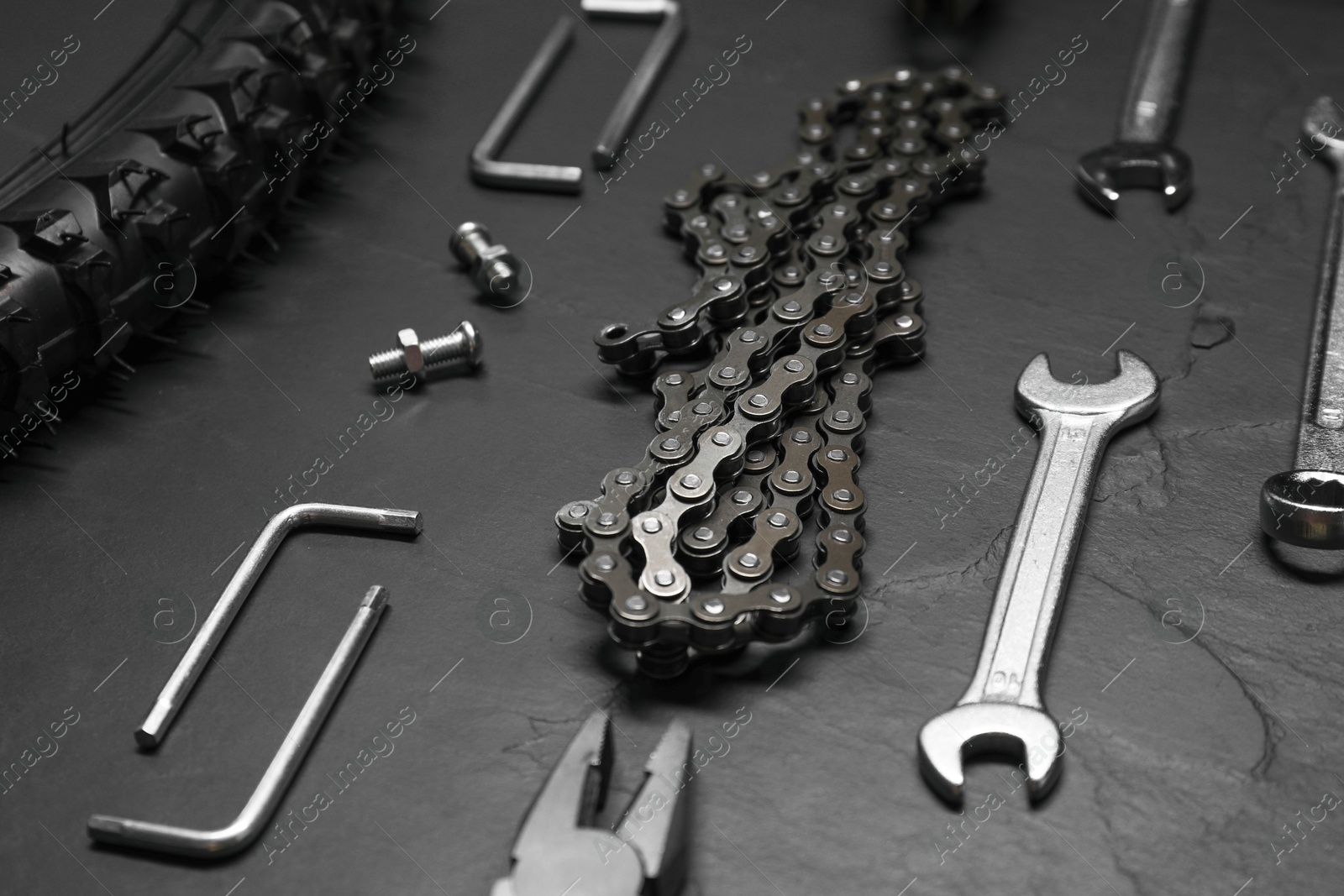 Photo of Wrenches, pliers, bicycle tire, chain and screws on dark gray textured background, closeup