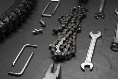 Wrenches, pliers, bicycle tire, chain and screws on dark gray textured background, closeup