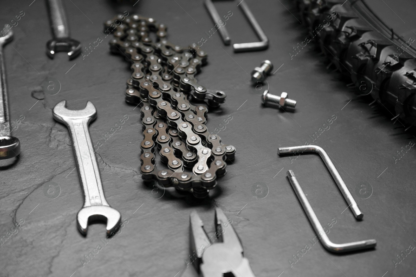 Photo of Wrenches, pliers, bicycle tire, chain and screws on dark gray textured background, closeup