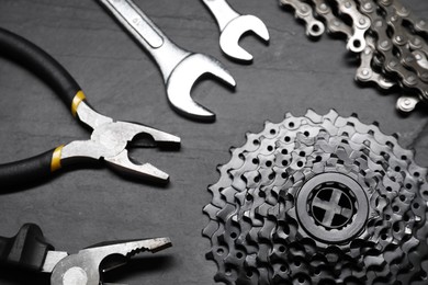 Photo of Wrenches, pliers, cassette and chain on dark gray textured background, above view