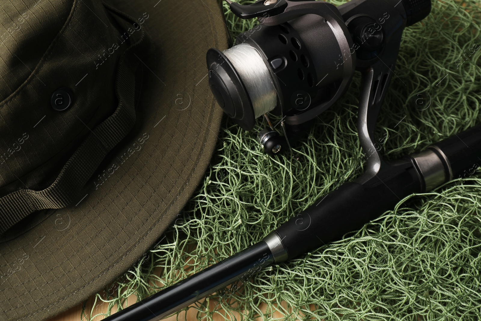 Photo of Fishing rod with spinning reel, hat and net on table, closeup