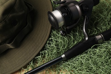 Fishing rod with spinning reel, hat and net on table, closeup