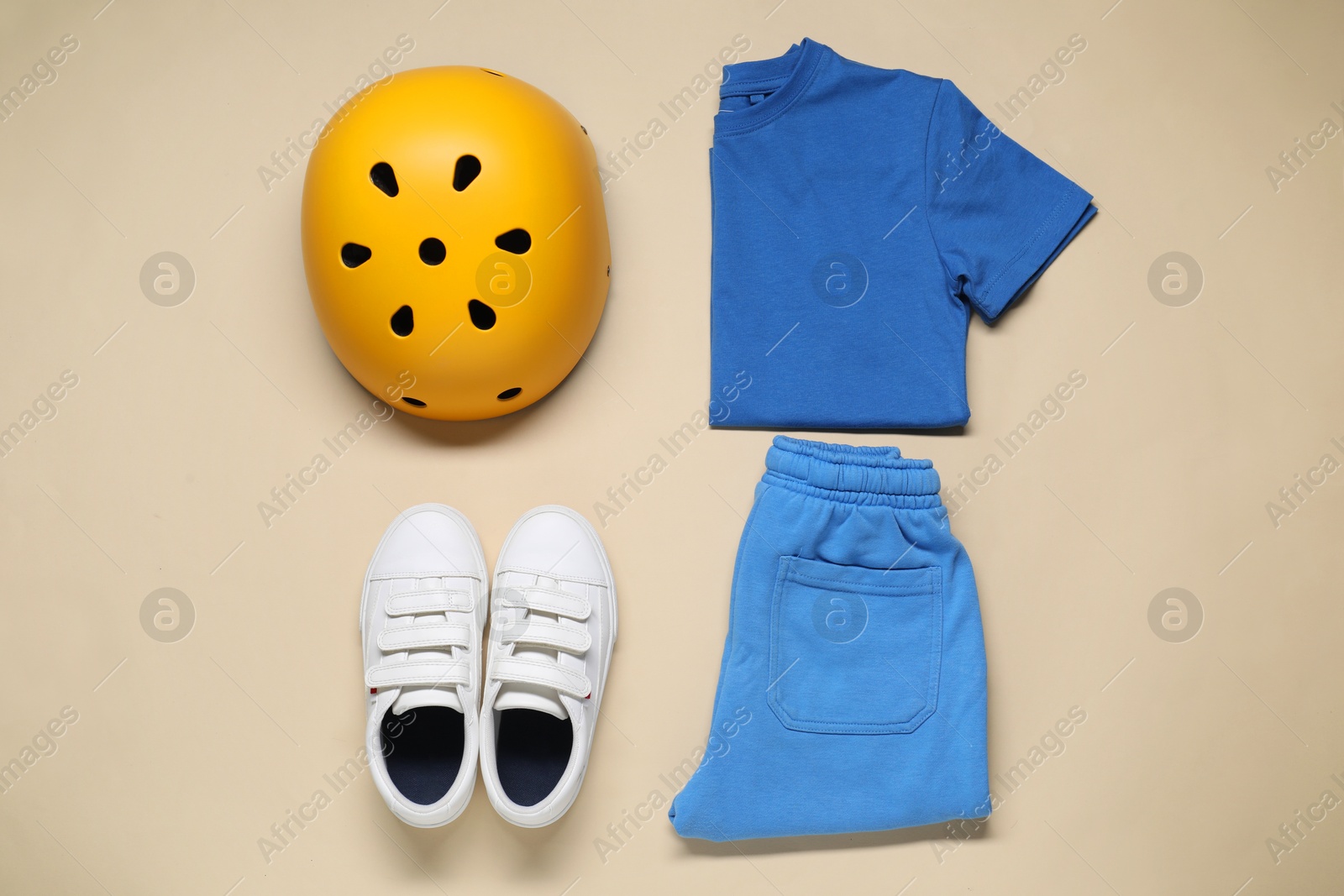 Photo of Bicycle helmet, sportswear and sneakers on beige background, flat lay