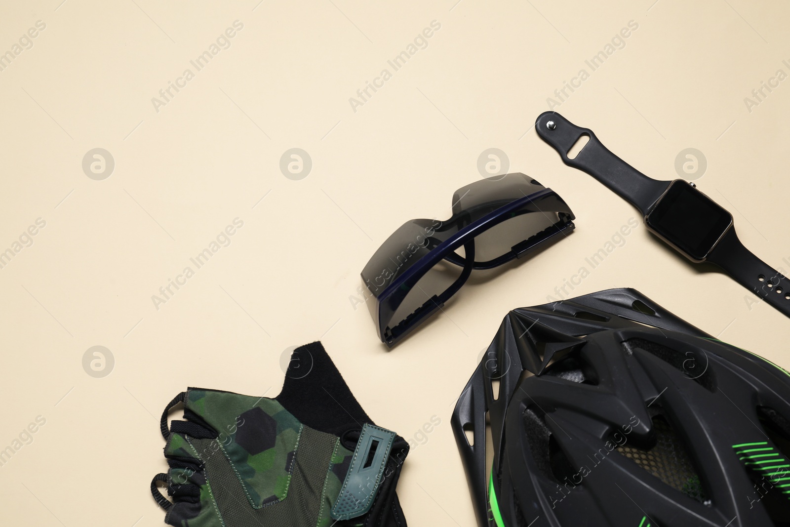 Photo of Bicycle helmet, fingerless cycling gloves, goggles and smartwatch on beige background, flat lay. Space for text