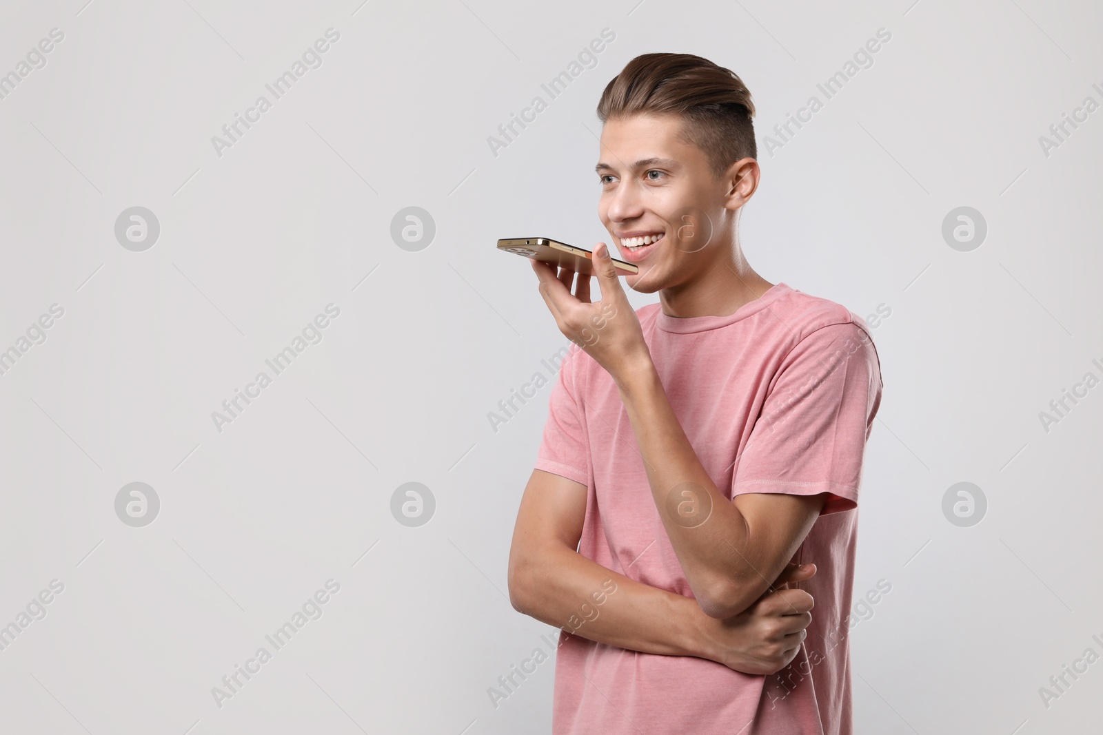 Photo of Young man recording voice message via smartphone on light gray background, space for text