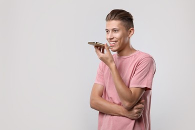 Photo of Young man recording voice message via smartphone on light gray background, space for text