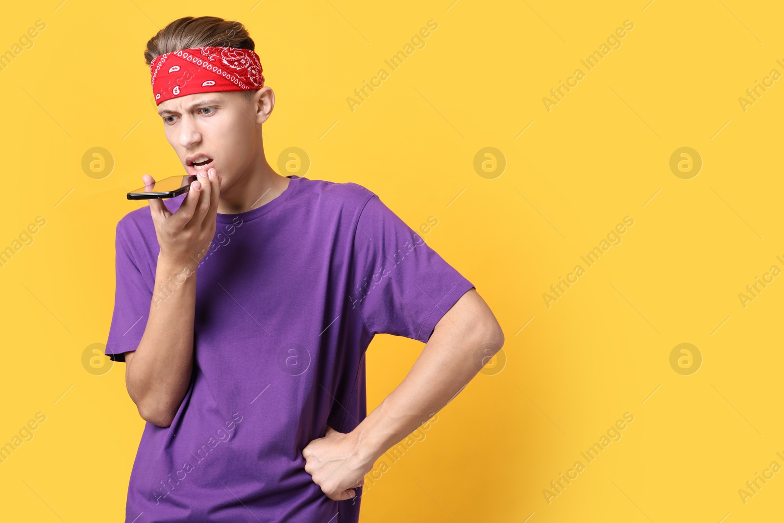 Photo of Young man recording voice message via smartphone on orange background, space for text