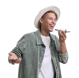 Young man in hat recording voice message via smartphone on white background