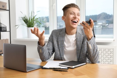 Photo of Young man recording voice message via smartphone in office