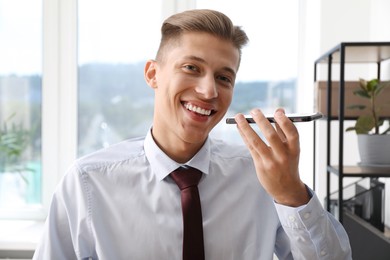 Young man with smartphone listening to voice message in office