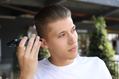 Young man with smartphone listening to voice message outdoors