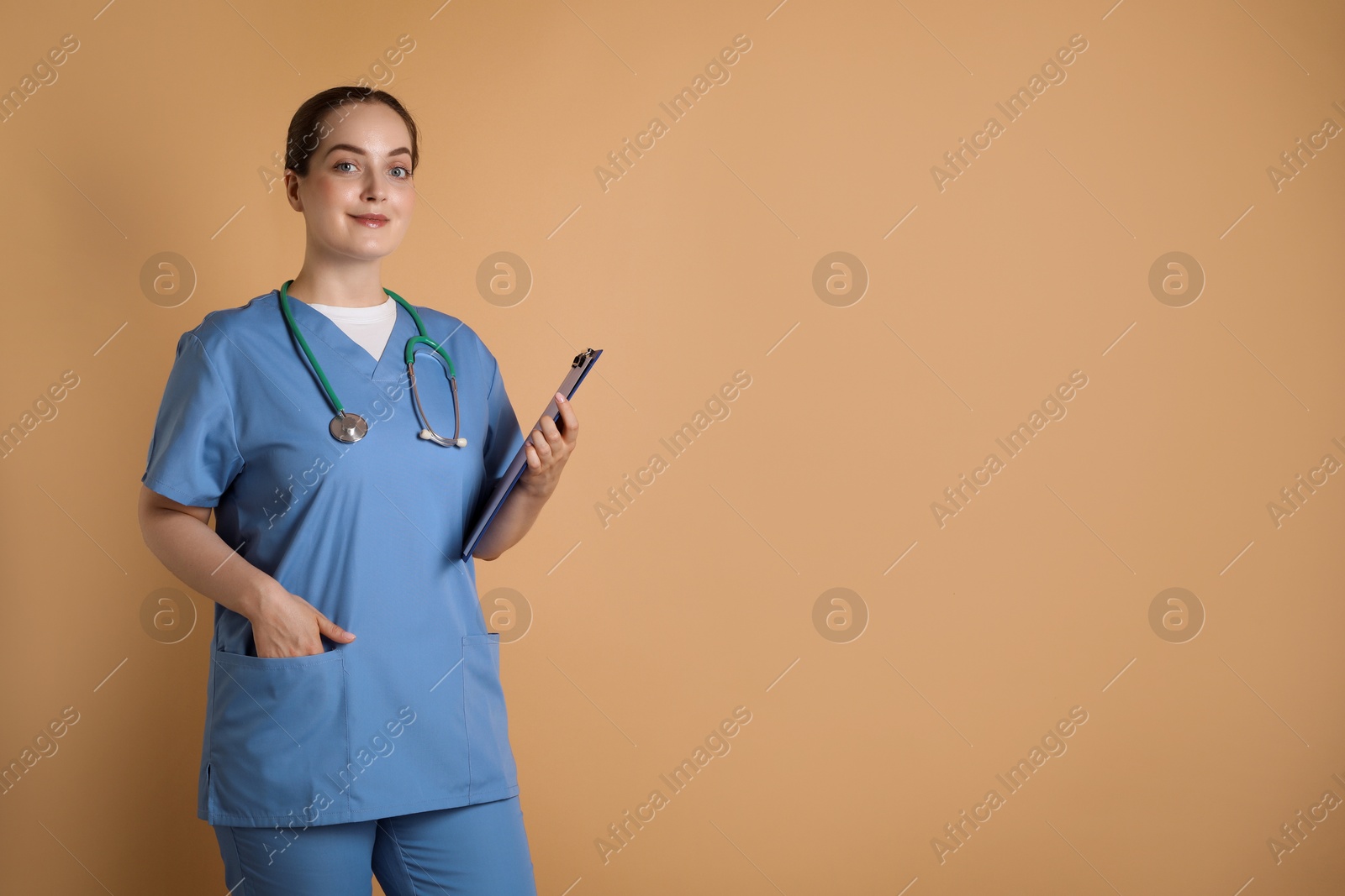 Photo of Portrait of professional nurse with stethoscope and clipboard on dark beige background