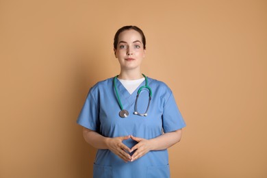 Portrait of professional nurse with stethoscope on dark beige background