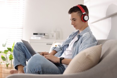 Teenage boy studying with laptop on sofa at home