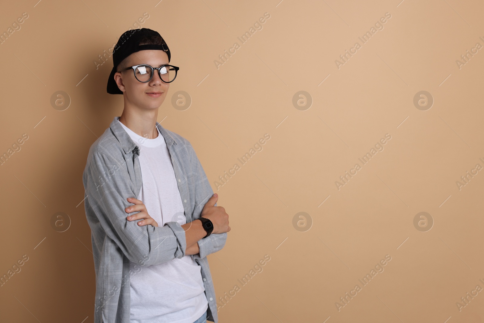 Photo of Portrait of teenage boy with crossed arms on dark beige background. Space for text