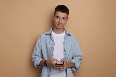 Photo of Portrait of teenage boy with smartphone on dark beige background