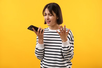 Photo of Emotional woman recording voice message via smartphone on yellow background