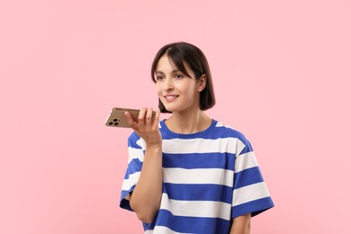 Beautiful woman recording voice message via smartphone on pink background