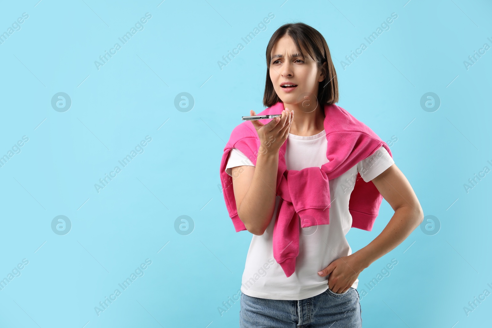 Photo of Beautiful woman recording voice message via smartphone on light blue background, space for text