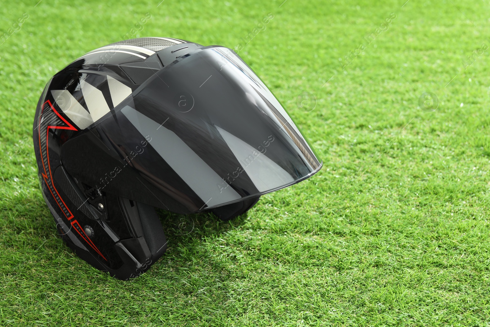 Photo of Modern motorcycle helmet with visor on green grass outdoors, space for text